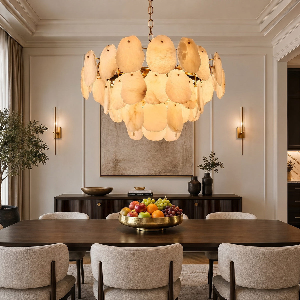 A modern minimalist dining room featuring a fruit bowl on a walnut table, framed by a luxury tiered alabaster stone chandelier and matching vertical wall sconces.