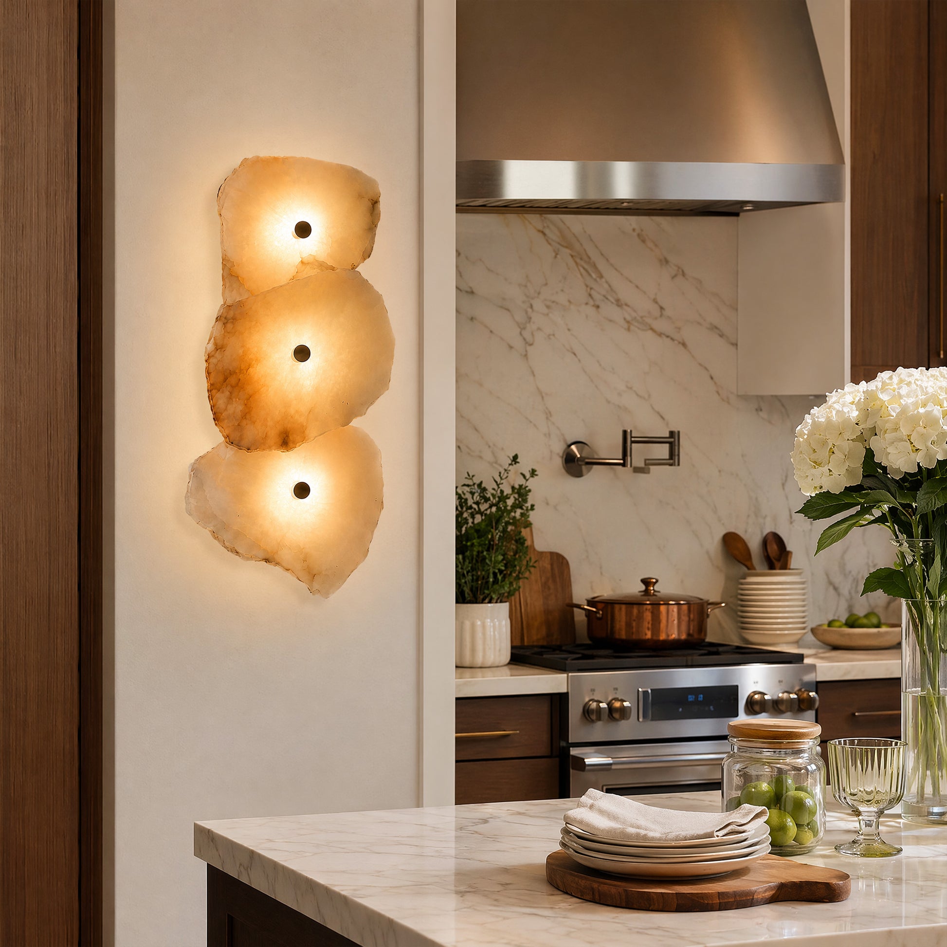 A warm and inviting modern kitchen backsplash area highlighting a 3-light natural stone alabaster wall sconce next to a stainless steel stove hood.
