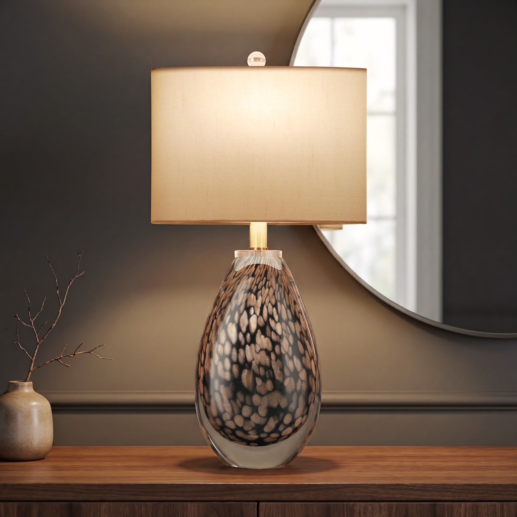 A minimalist foyer setup featuring an illuminated dragon scale art glass lamp on a wooden credenza in front of a large circular wall mirror.
