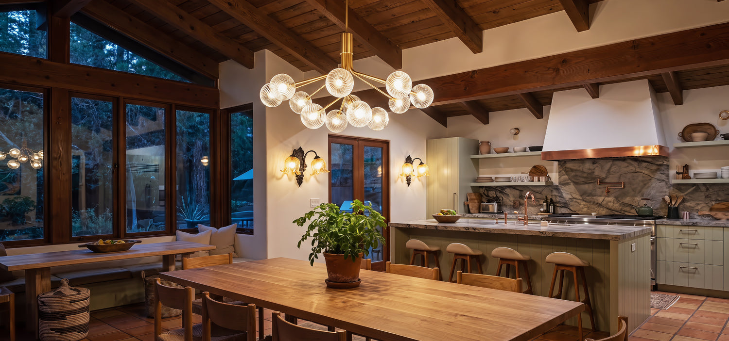 An elegant modern organic dining area showcasing a linear brushed brass chandelier suspended above the dining table and vintage iron sconces emitting warm, symmetric light arcs on plaster walls.