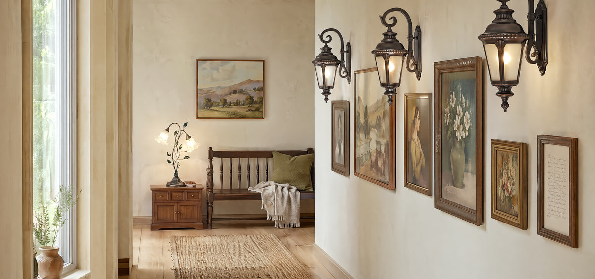 An organic modern hallway gallery wall featuring vintage iron sconces and a matching iron table lamp on a rustic wooden bench under soft natural daylight.
