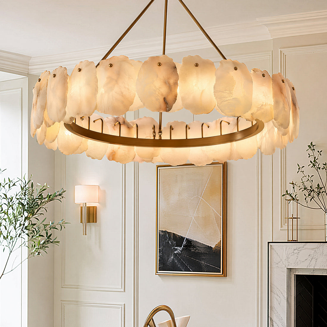 A close up view of a round Spanish alabaster stone slab chandelier lit during the day inside a sophisticated cream toned living room with a white marble fireplace.