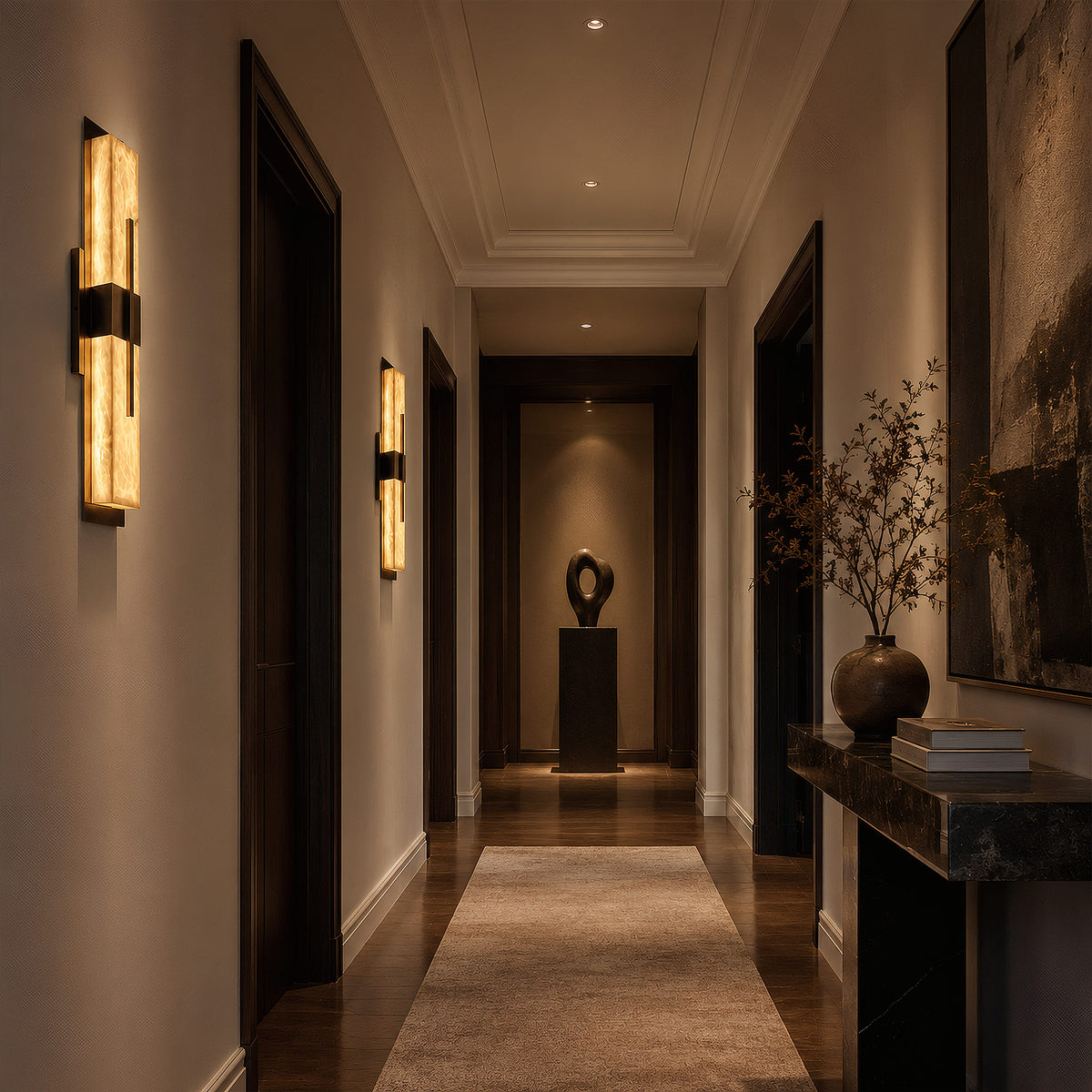 A dramatic, moody hallway in a luxury home with dark wood doors, featuring two glowing linear alabaster wall sconces washing warm light over a stone console table and a sculpture.