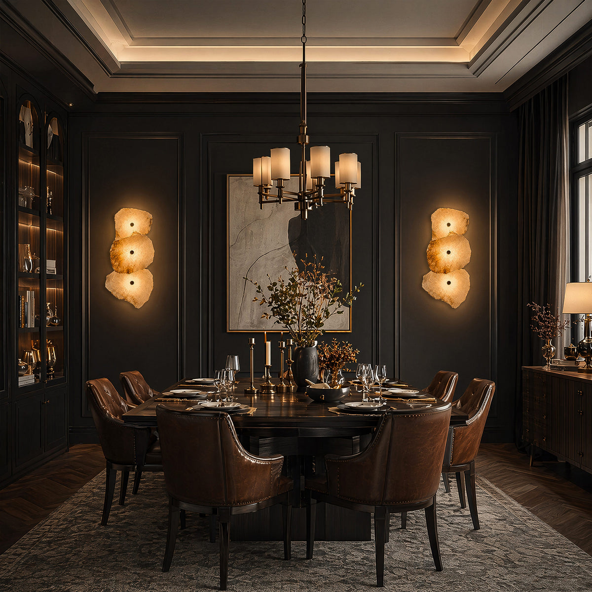 A dramatic, dark-toned quiet luxury dining room with a grand table, leather chairs, and two warm alabaster wall sconces mounted on deep charcoal walls.