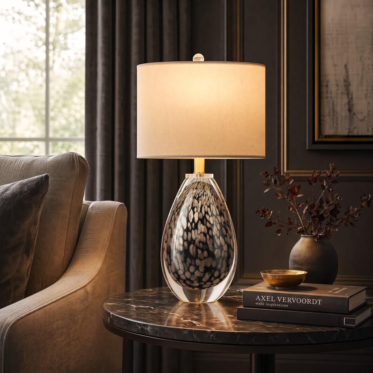 A moody dark academic style living room corner highlighting a glowing dragon egg textured glass lamp on a black marble side table with stacked design books.
