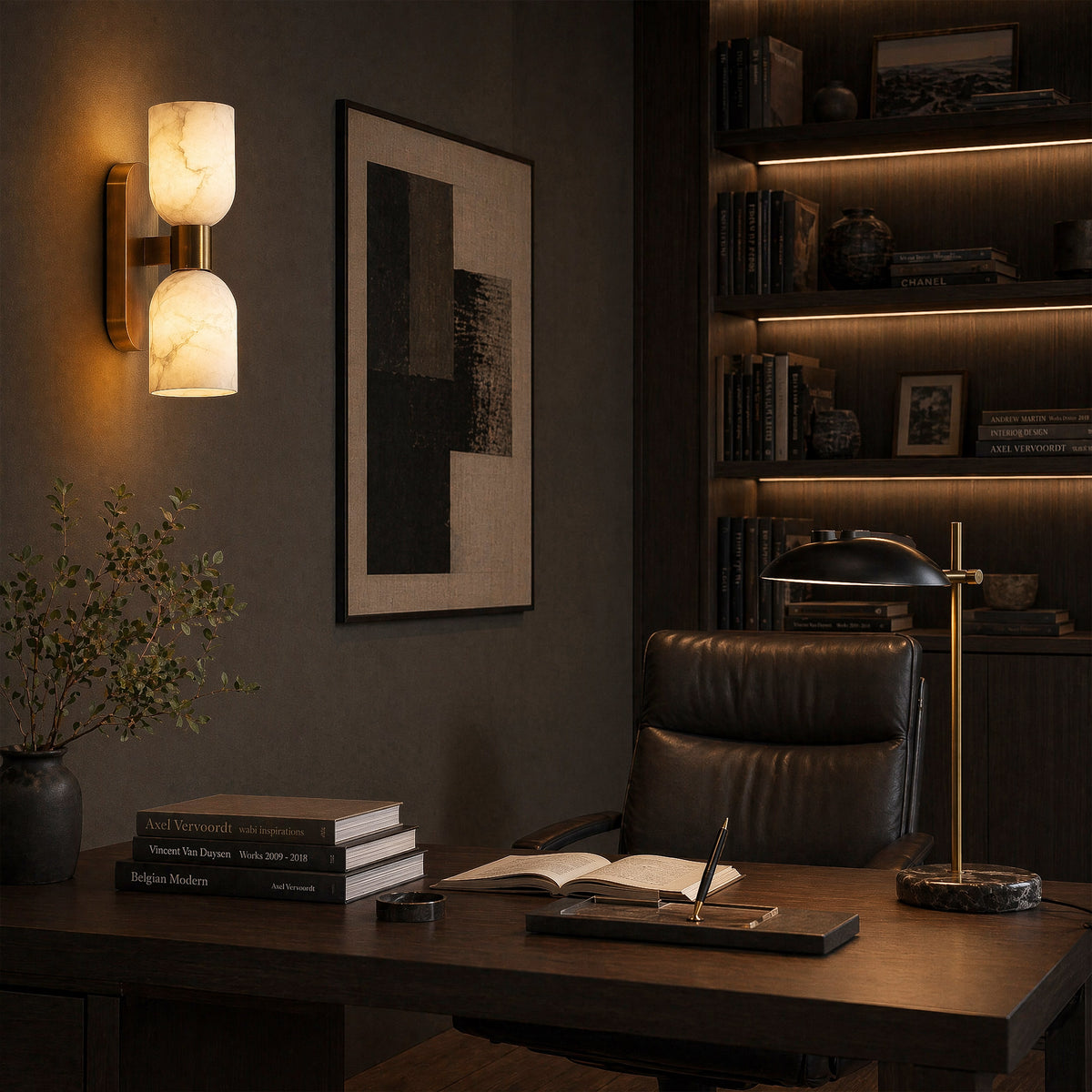 A quiet luxury home office with a dark wood desk, a leather chair, a mid-century desk lamp, and a dual-light alabaster stone wall fixture casting a soft glow against a charcoal gray wall.