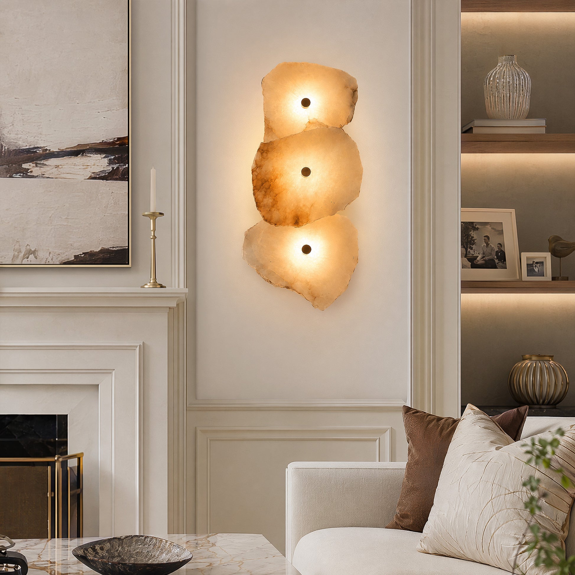 A warm, sophisticated living room with a classic fireplace and a 3-light alabaster stone wall sconce casting a cozy amber glow next to a neutral fabric sofa.