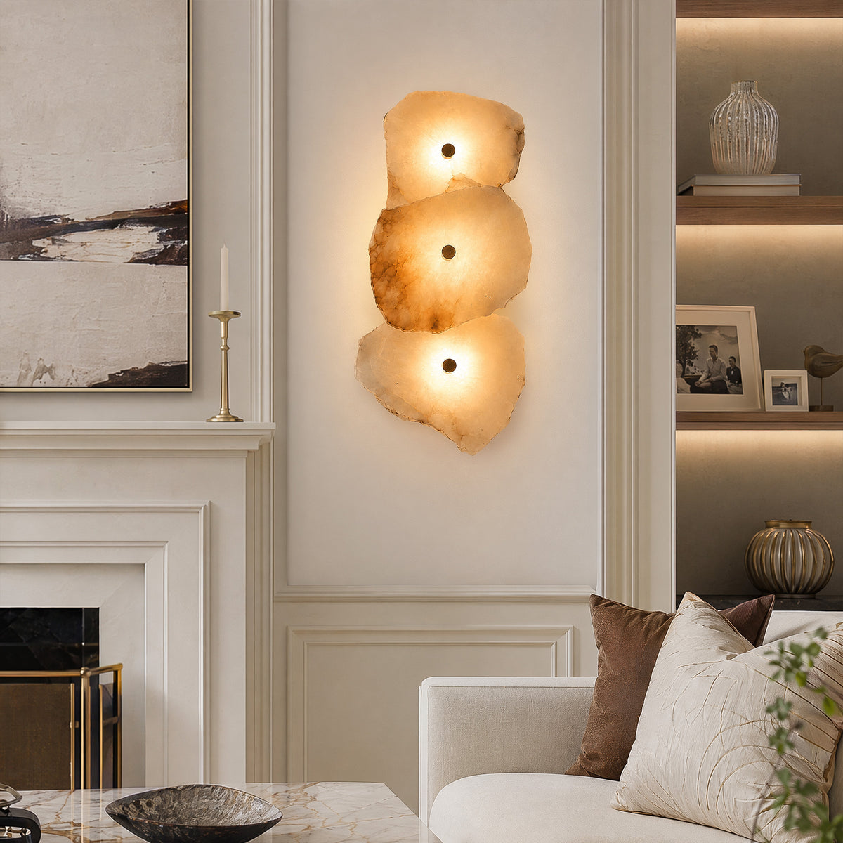 A warm, sophisticated living room with a classic fireplace and a 3-light alabaster stone wall sconce casting a cozy amber glow next to a neutral fabric sofa.