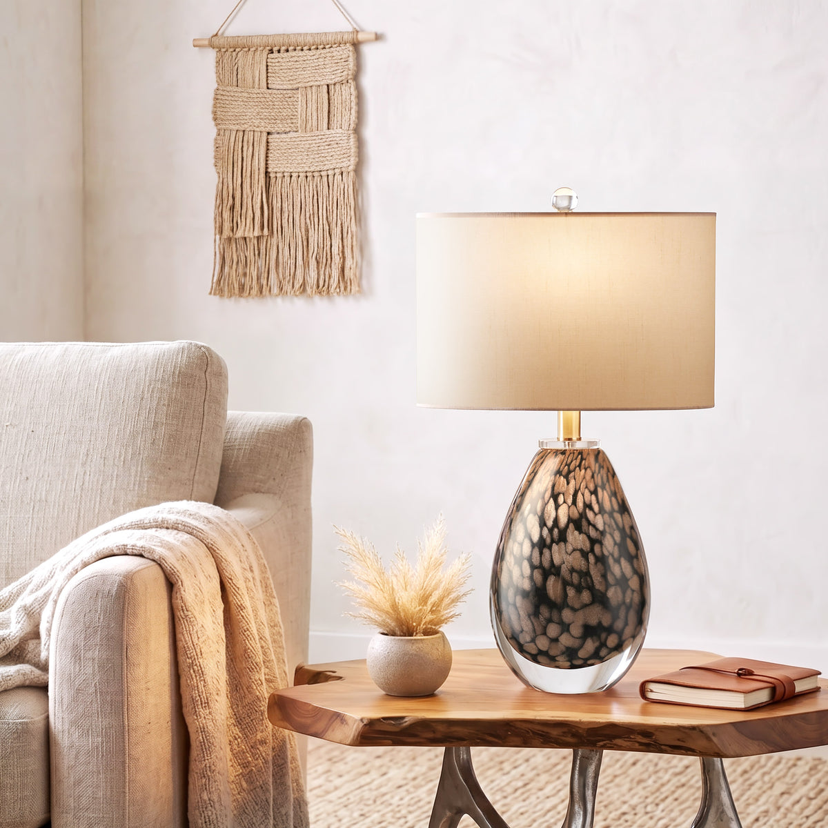 An organic modern living room corner featuring a lit Murano style glass table lamp with gold brown dragon egg scales on a live edge wooden side table next to a linen sofa.