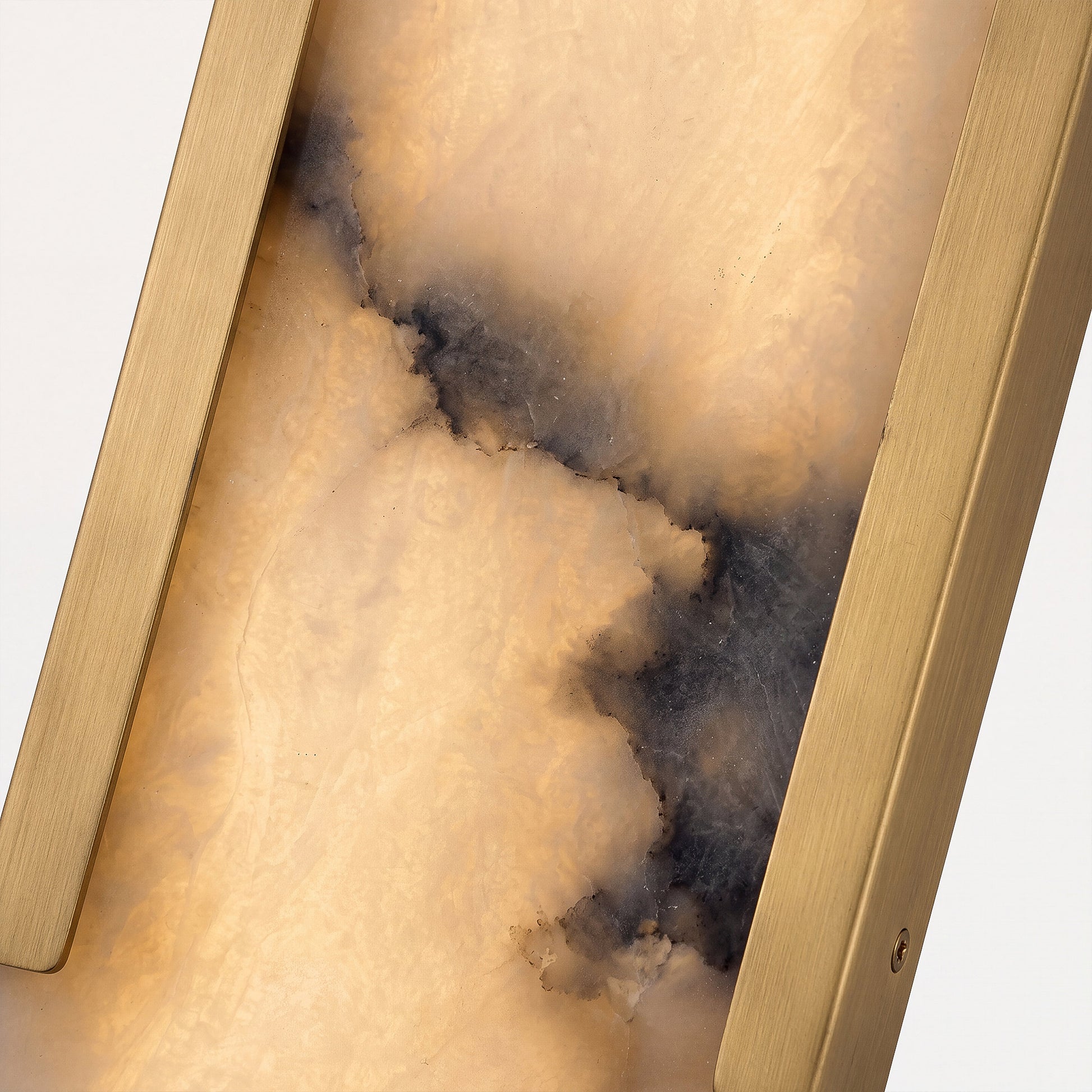 Macro detail shot of a premium wall light showcasing the rich natural dark veining within the translucent Spanish alabaster stone and the heavy solid brass side frame.