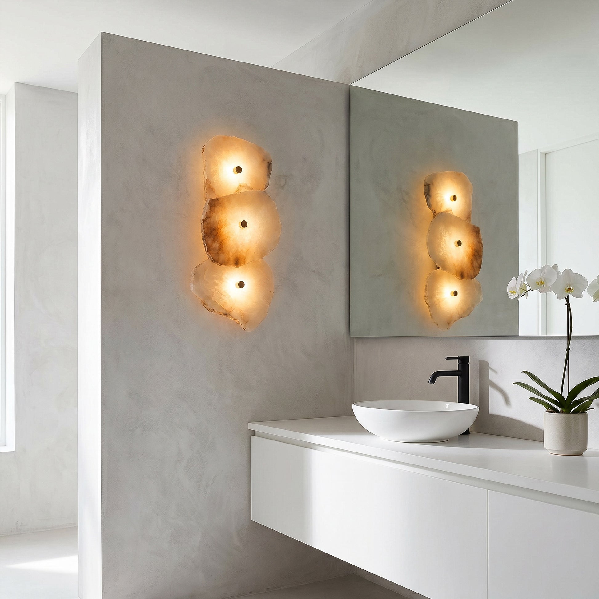 An elegant, minimalist concrete bathroom vanity showcasing a vertical alabaster stone wall sconce next to a sleek black faucet and white vessel sink.