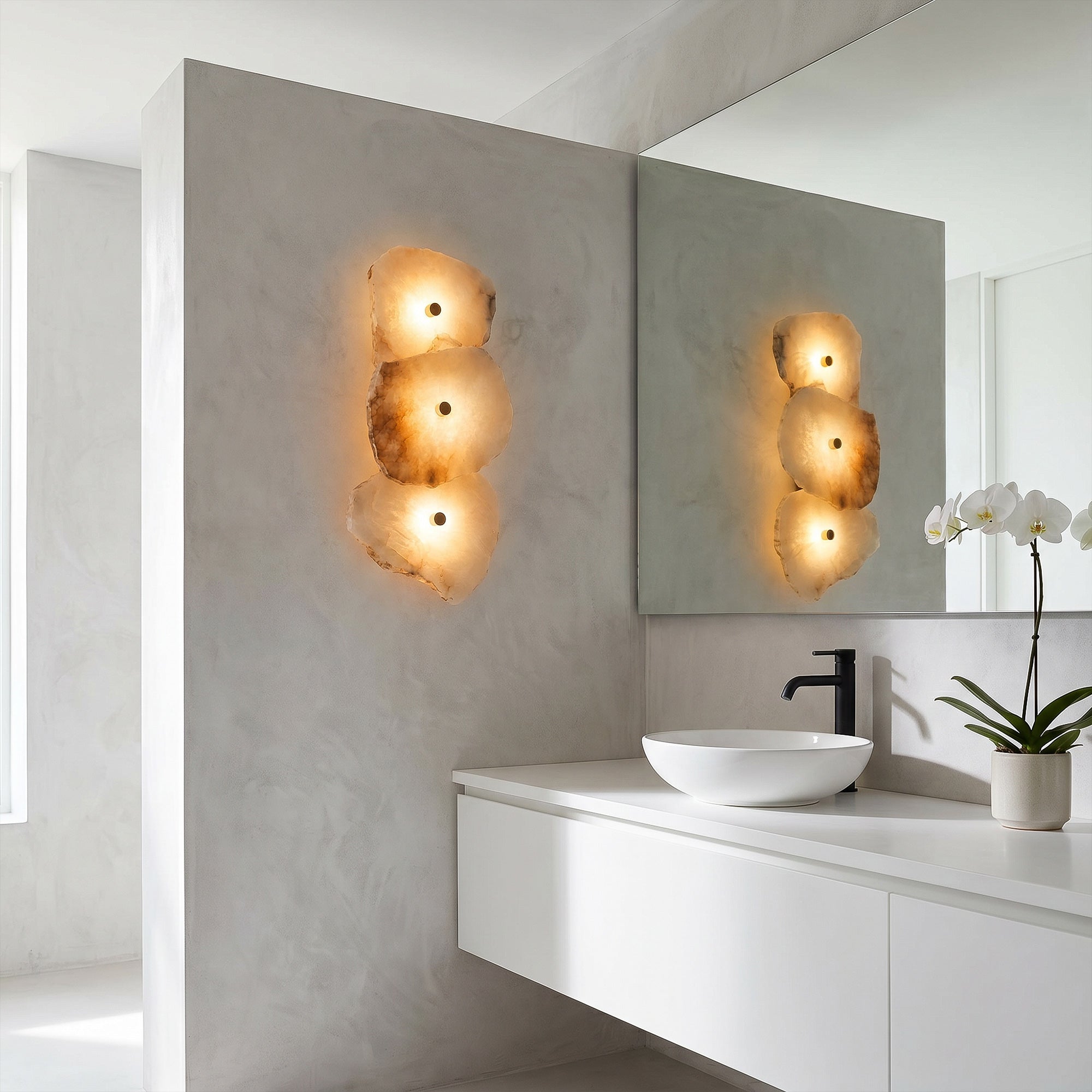 An elegant, minimalist concrete bathroom vanity showcasing a vertical alabaster stone wall sconce next to a sleek black faucet and white vessel sink.