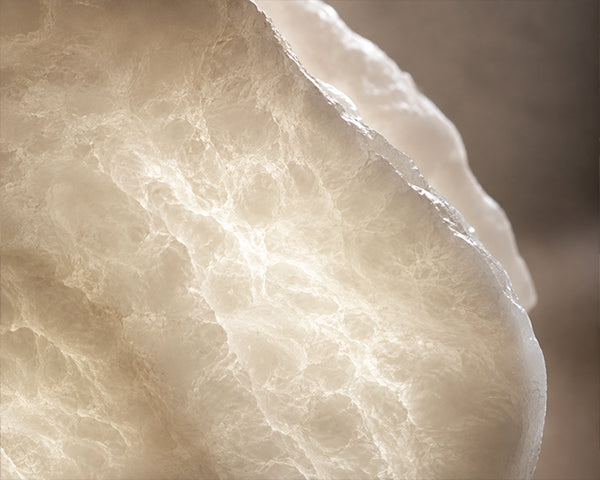 Extreme close up macro view of illuminated natural spanish alabaster stone showing organic mineral veining and soft translucent glow.
