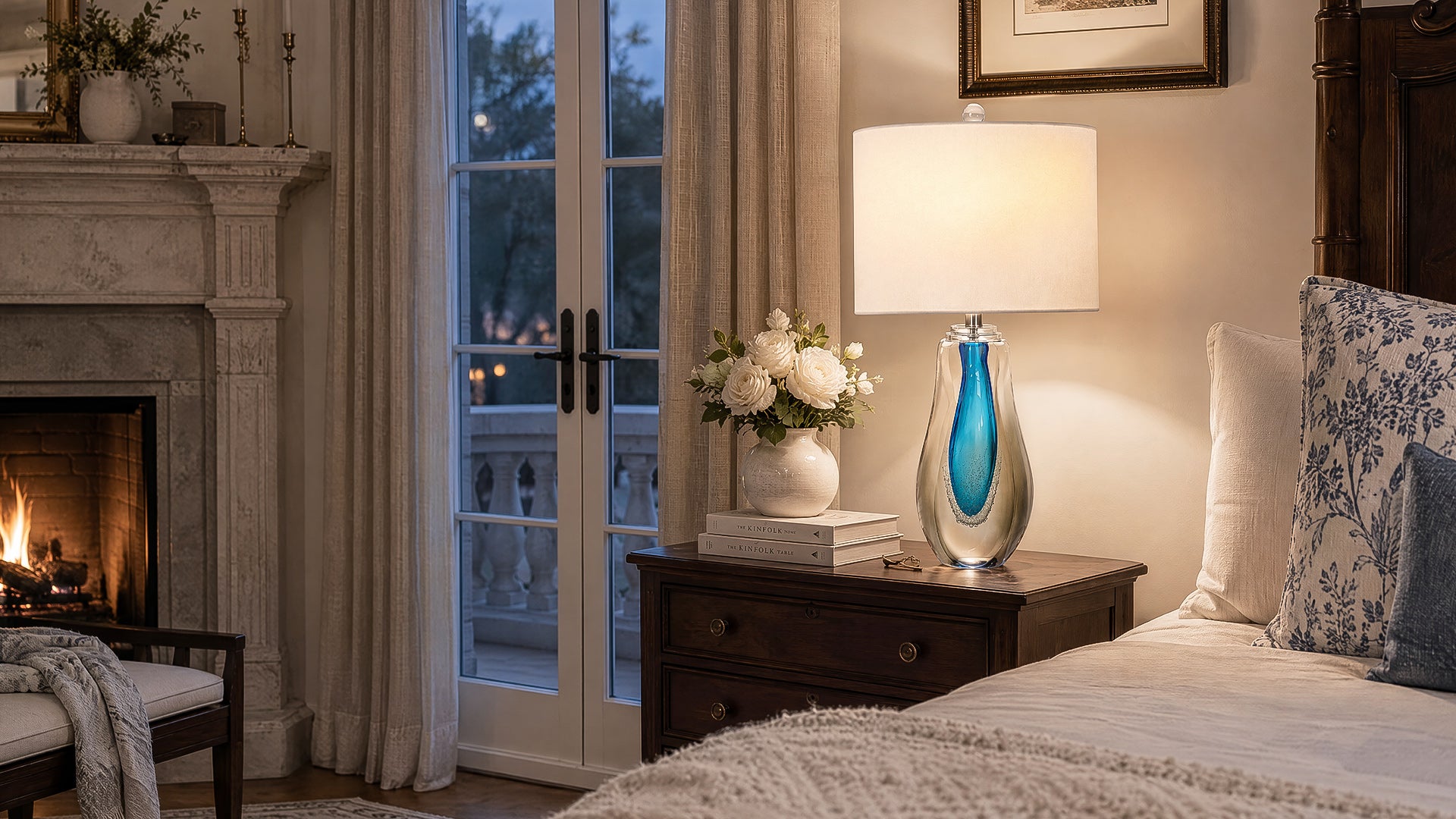 Art glass table lamp emitting warm ambient light on a nightstand in a luxury bedroom setting