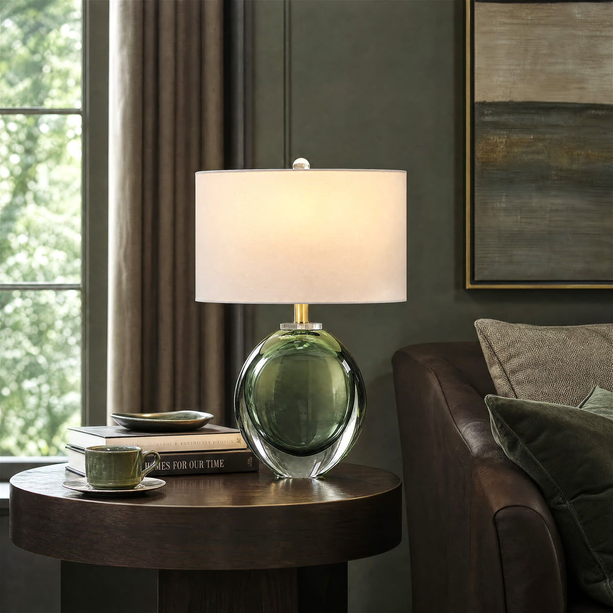 Warmly lit moss green bubble glass lamp on a dark wood accent table next to a luxury brown leather sofa in a moody olive green wall living room
