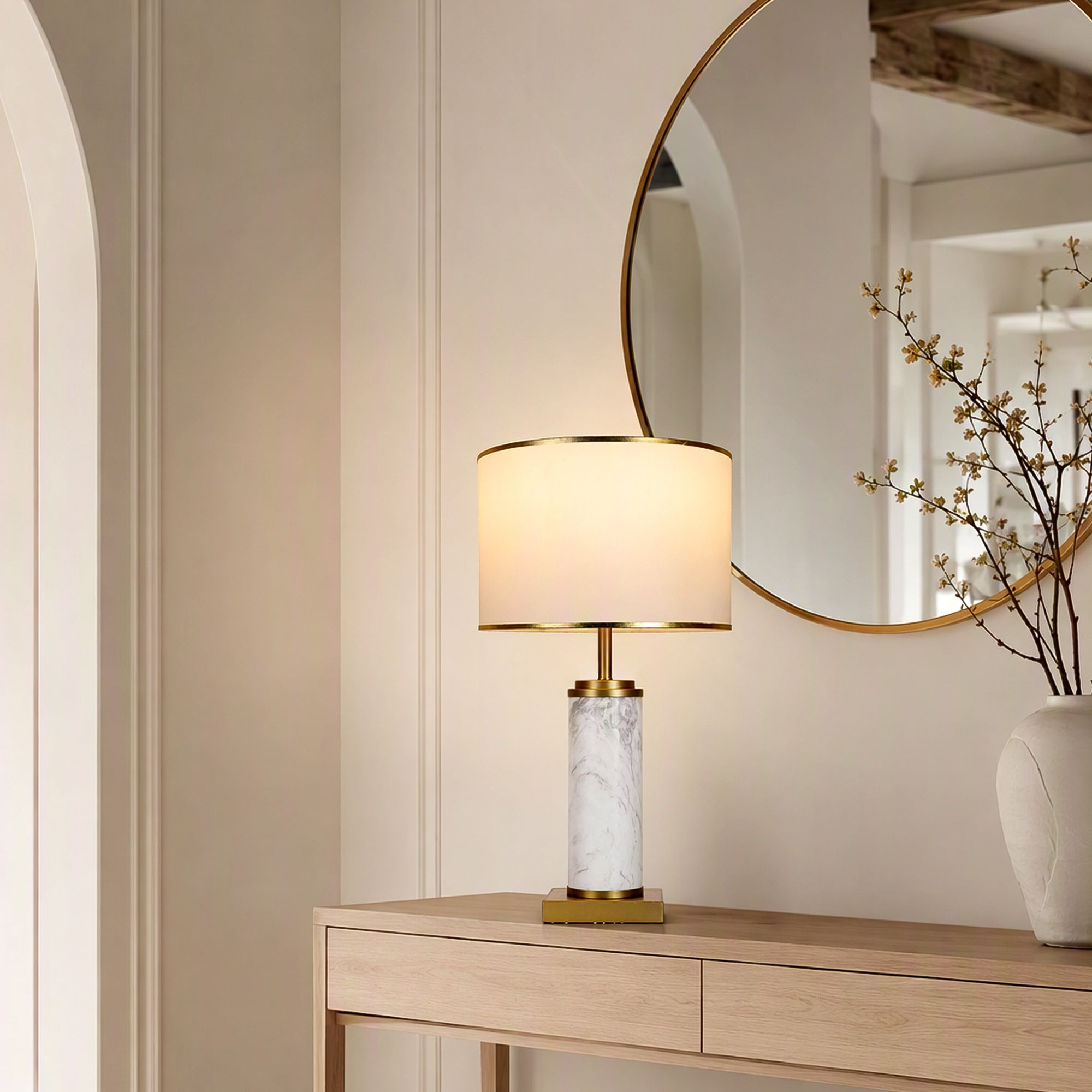 Illuminated white marble cylinder table lamp on light wood console table in minimalist hallway