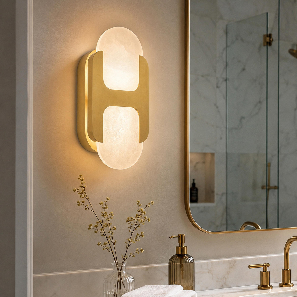 Illuminated solid brass H-frame Spanish alabaster wall sconce mounted next to a bathroom mirror on a light neutral wall
