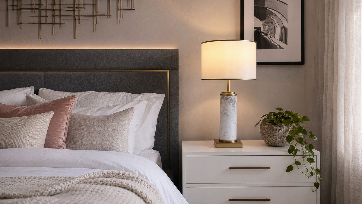 Illuminated white marble cylinder table lamp on white nightstand in contemporary bedroom setting