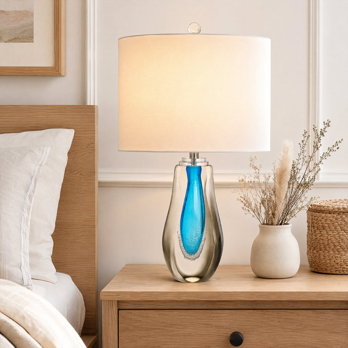 Illuminated art glass table lamp on a light wood bedside table in a bright minimalist bedroom