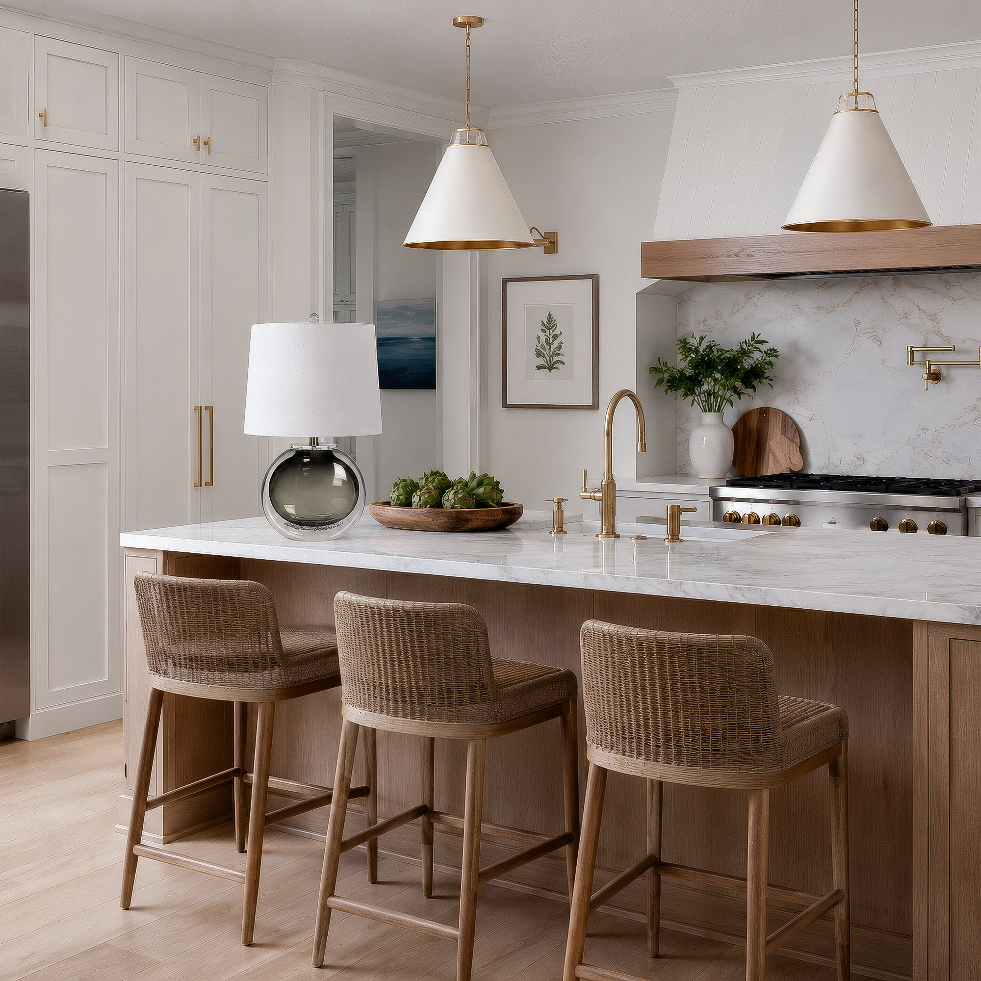 Art glass table lamp placed on a marble kitchen island with rattan bar stools and white pendant lights