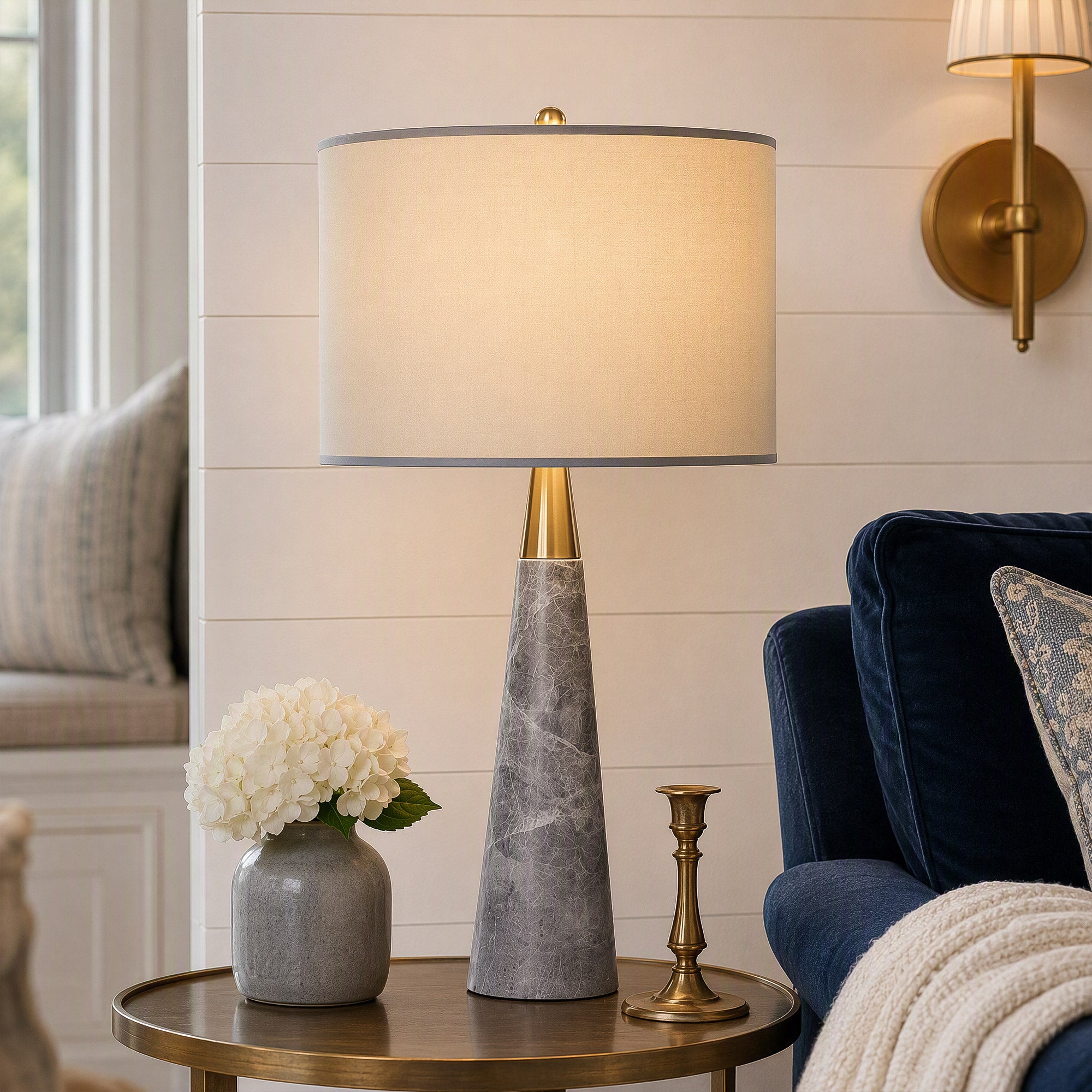 Illuminated grey marble cone table lamp on brass side table next to navy blue velvet sofa