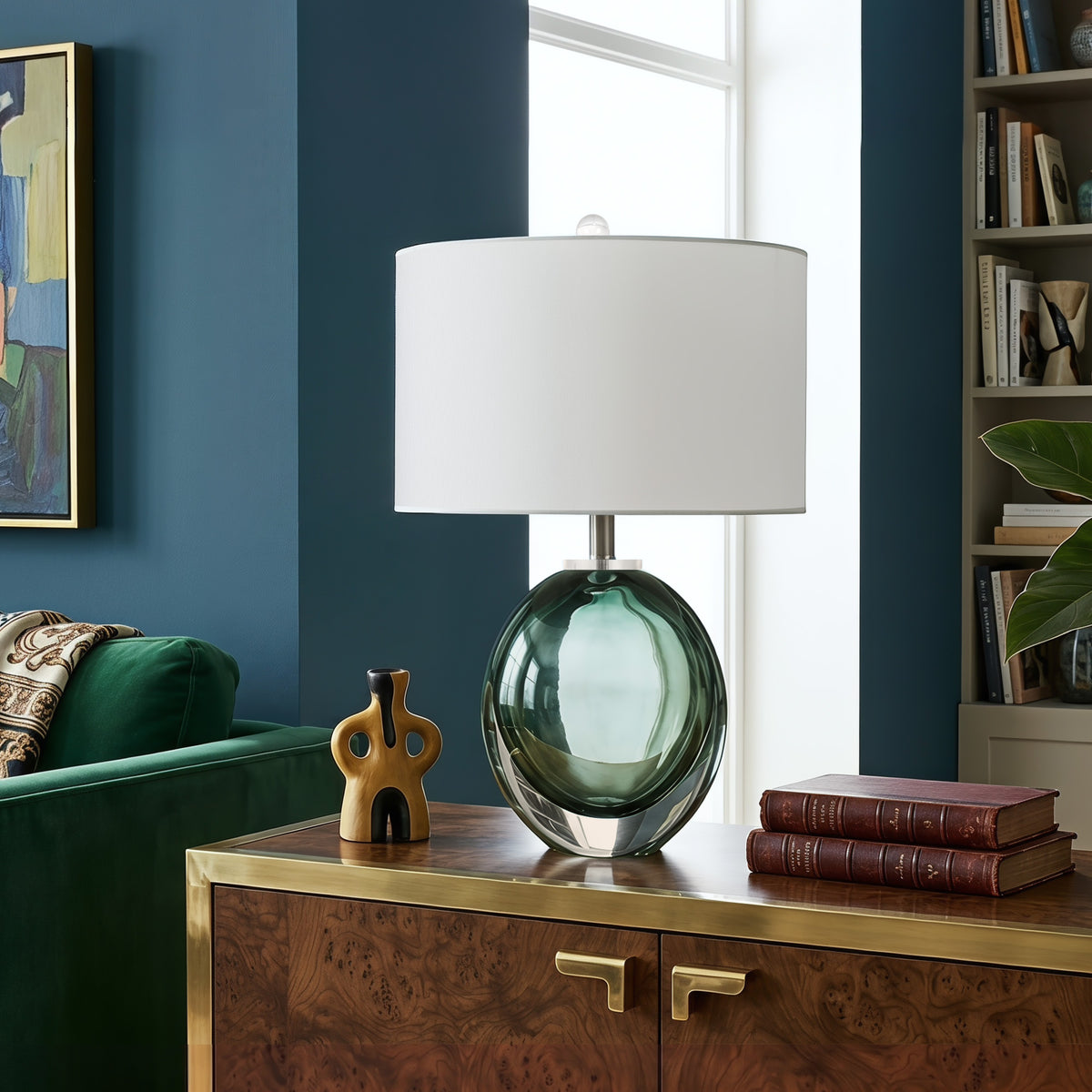 Murano style sage green fluid bubble glass lamp lit up on a premium burl wood cabinet next to an avocado green velvet armchair in a retro chic living room