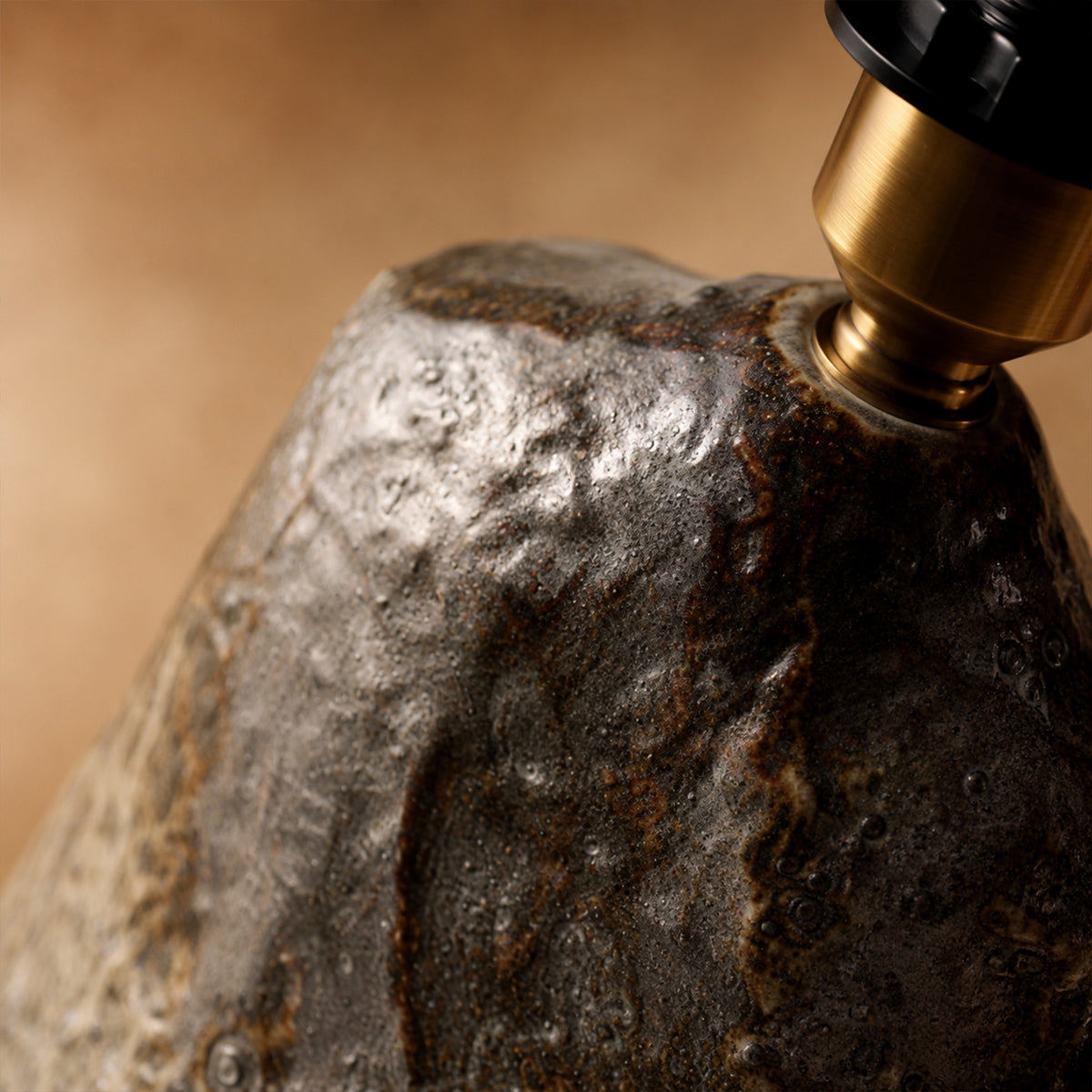 Close up view of the top of a rockery ceramic lamp body showing a volcanic metallic flambe glaze texture and brass socket hardware.