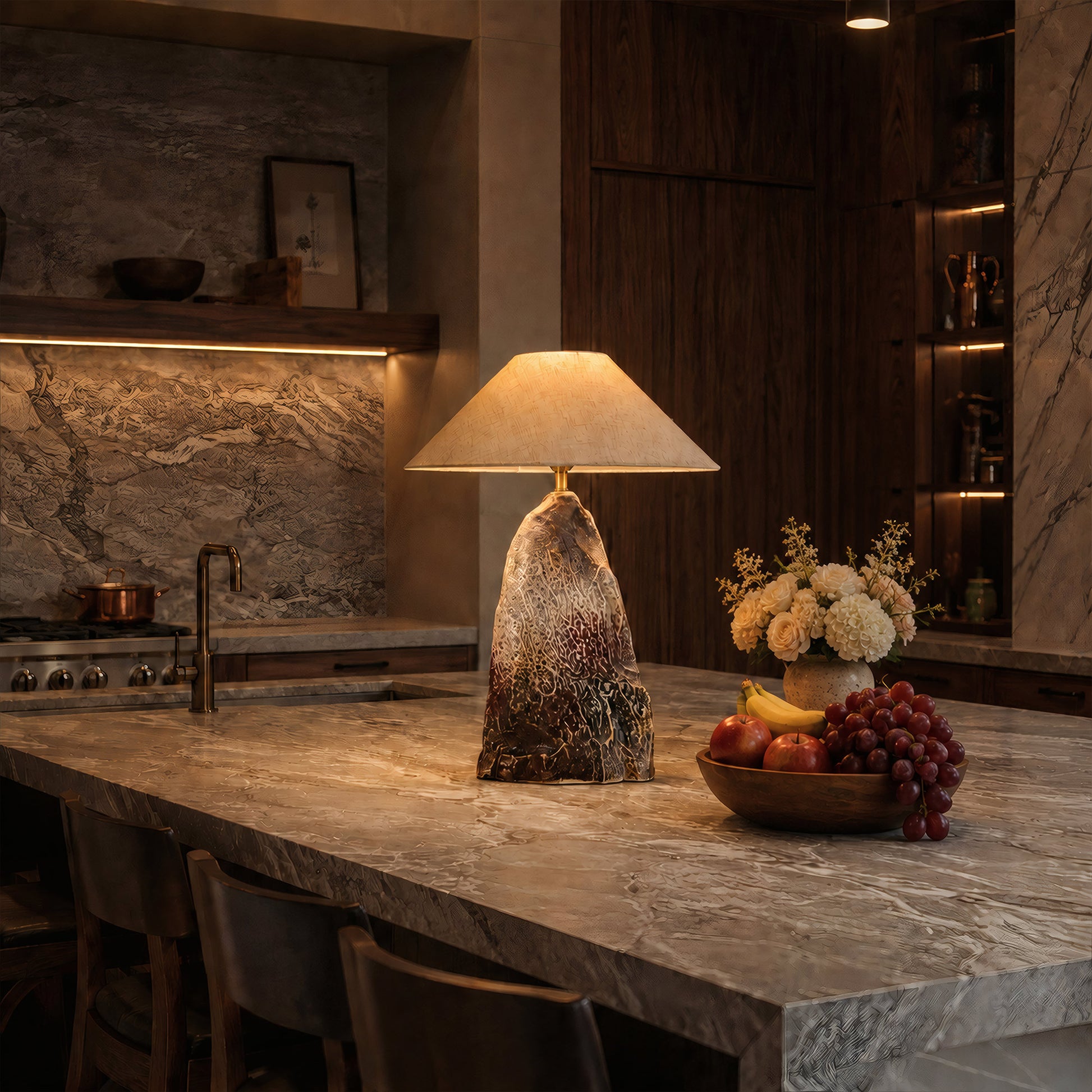 Warmly lit rockery ceramic table lamp styled on a large marble kitchen island counter next to a bowl of fresh fruit.