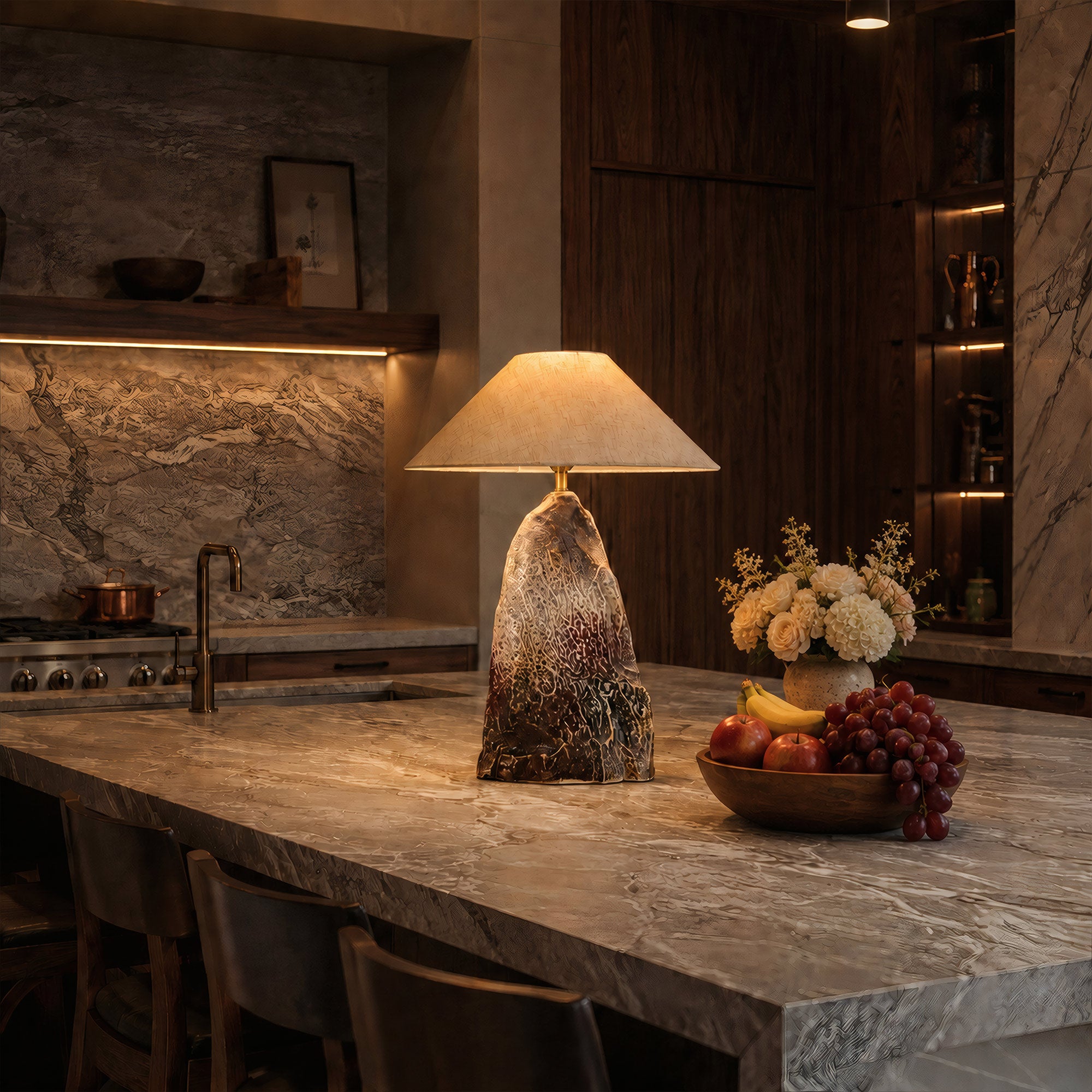 Warmly lit rockery ceramic table lamp styled on a large marble kitchen island counter next to a bowl of fresh fruit.