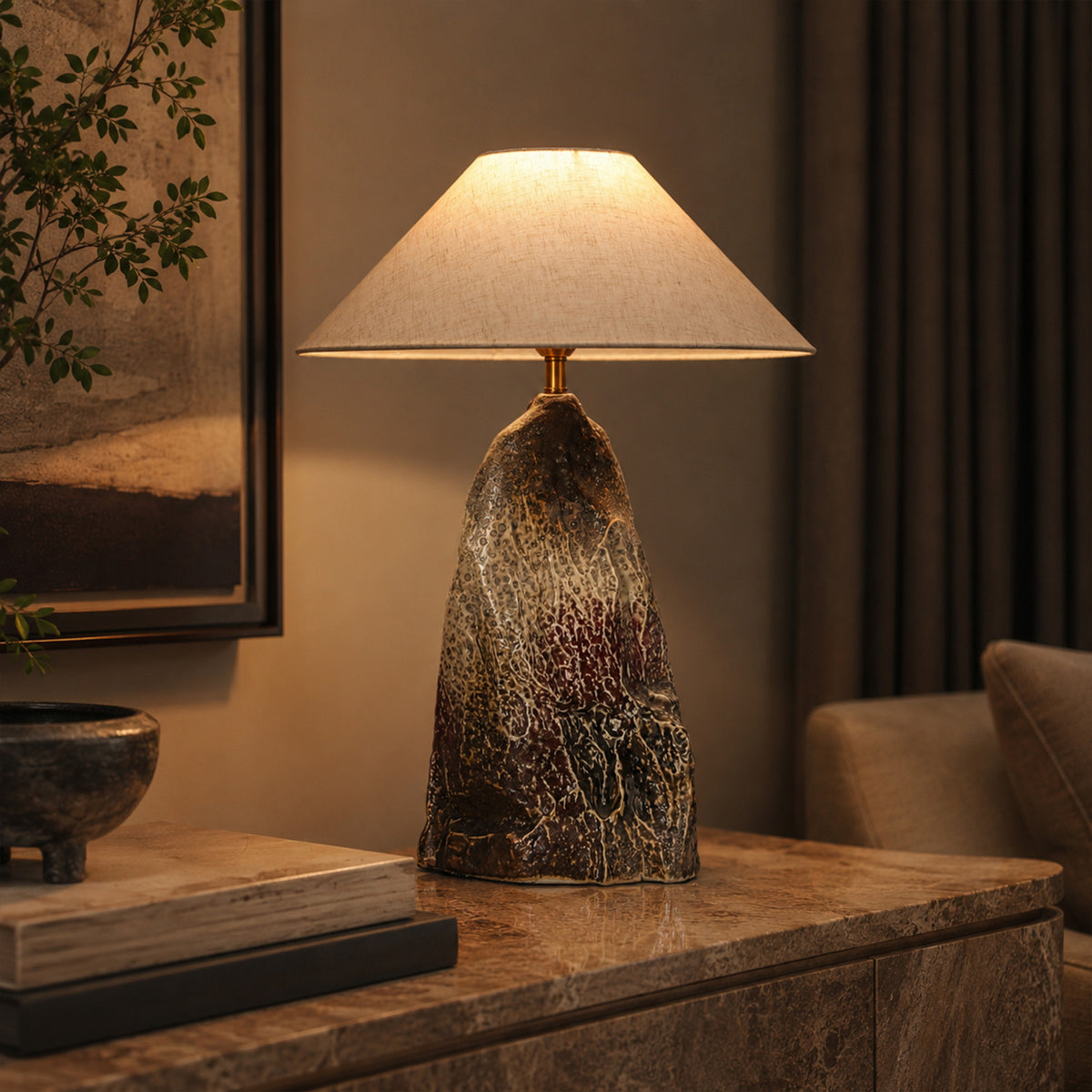 Illuminated rockery ceramic table lamp casting warm light on a marble credenza console table in a cozy evening living room setting.