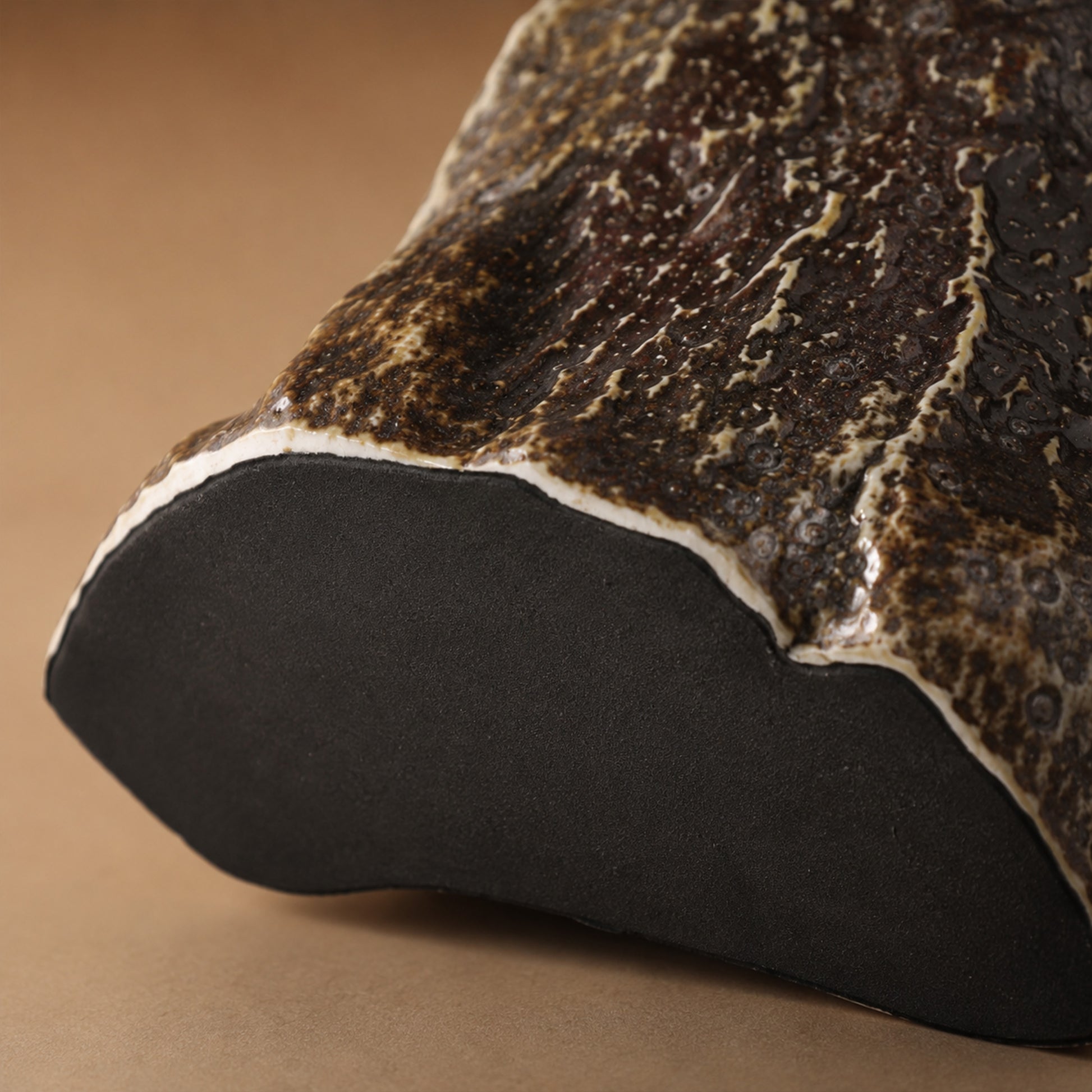 Close up detail of the raw dark clay base and rough flambe glaze texture on the lower section of a rockery ceramic table lamp.