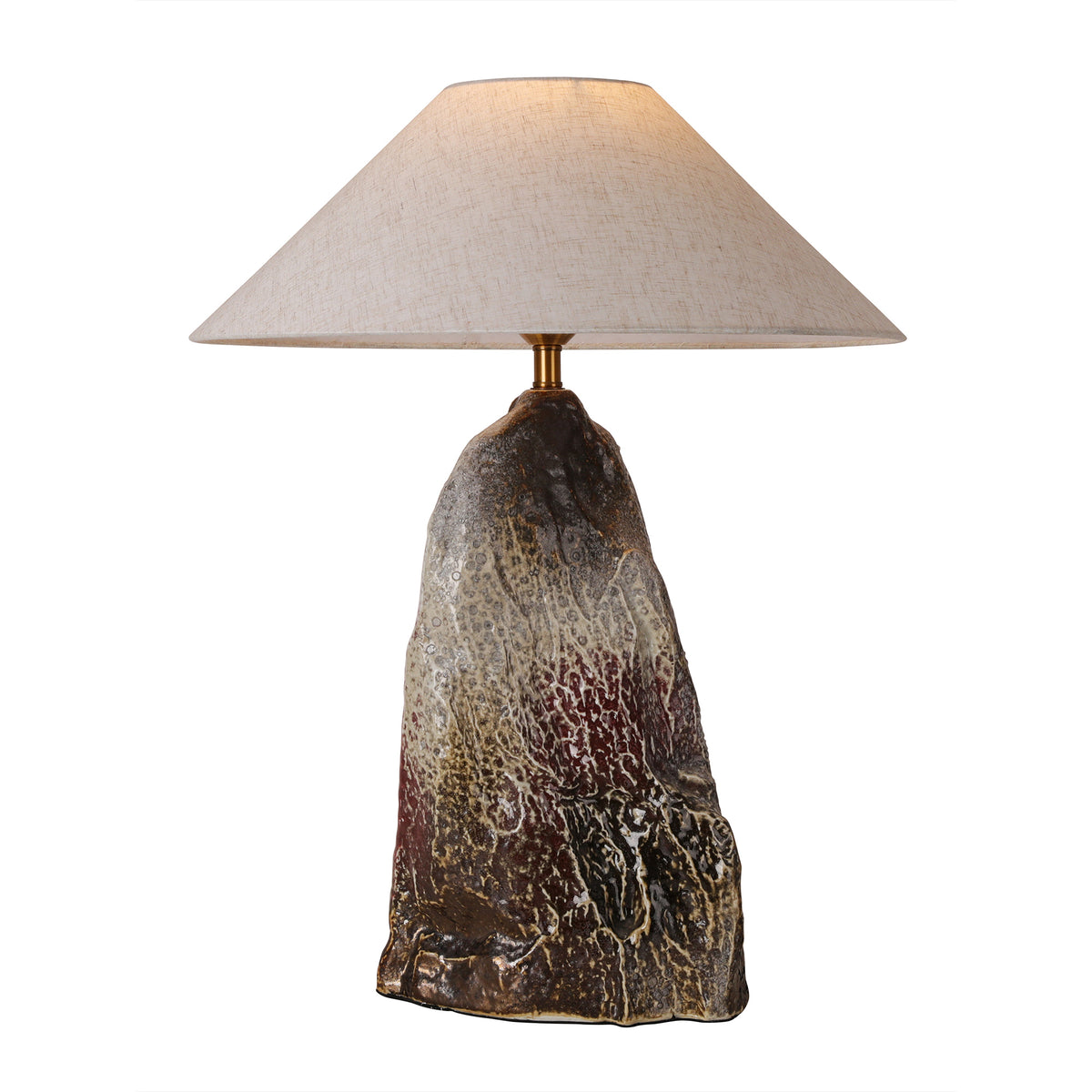 Artistic rockery flambe glaze ceramic table lamp with a tapered linen shade illuminated against a pure white background.