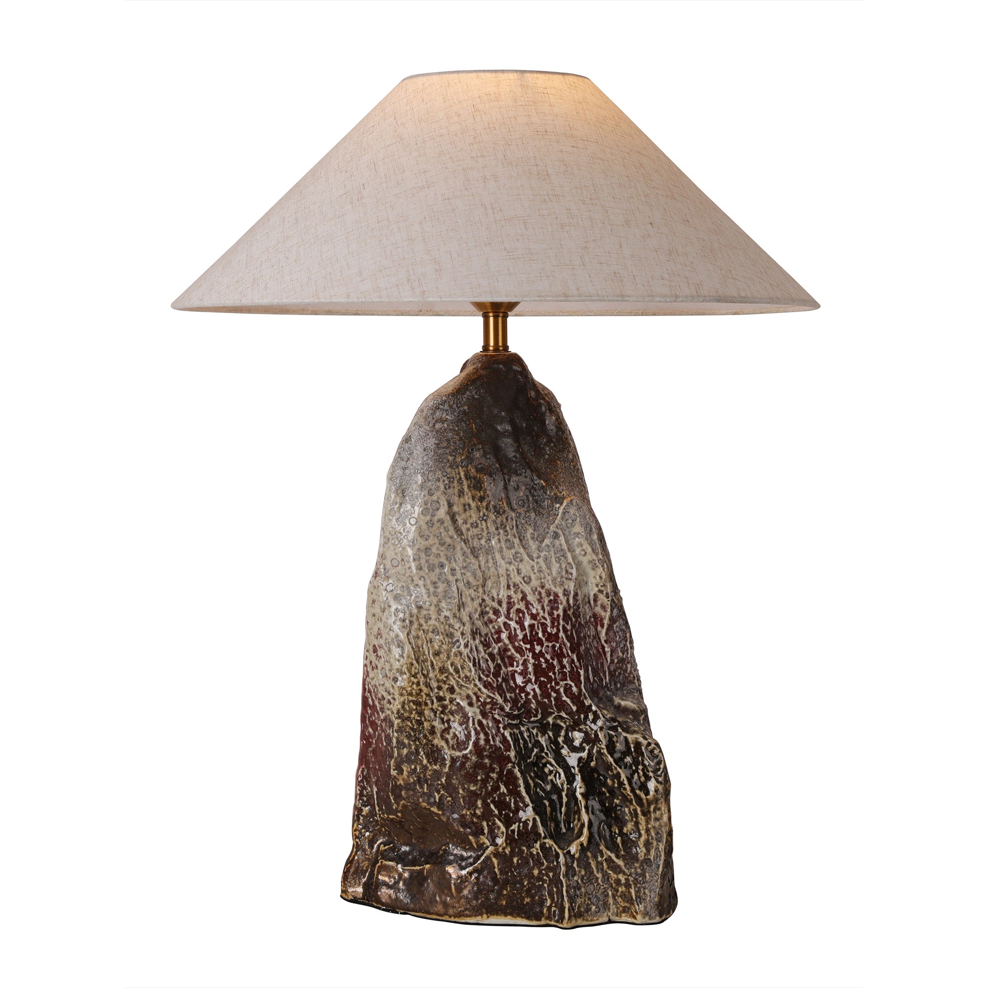 Artistic rockery flambe glaze ceramic table lamp with a tapered linen shade illuminated against a pure white background.