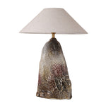 Artistic rockery flambe glaze ceramic table lamp with an unlit organic rock shape body and fabric shade on a white background.
