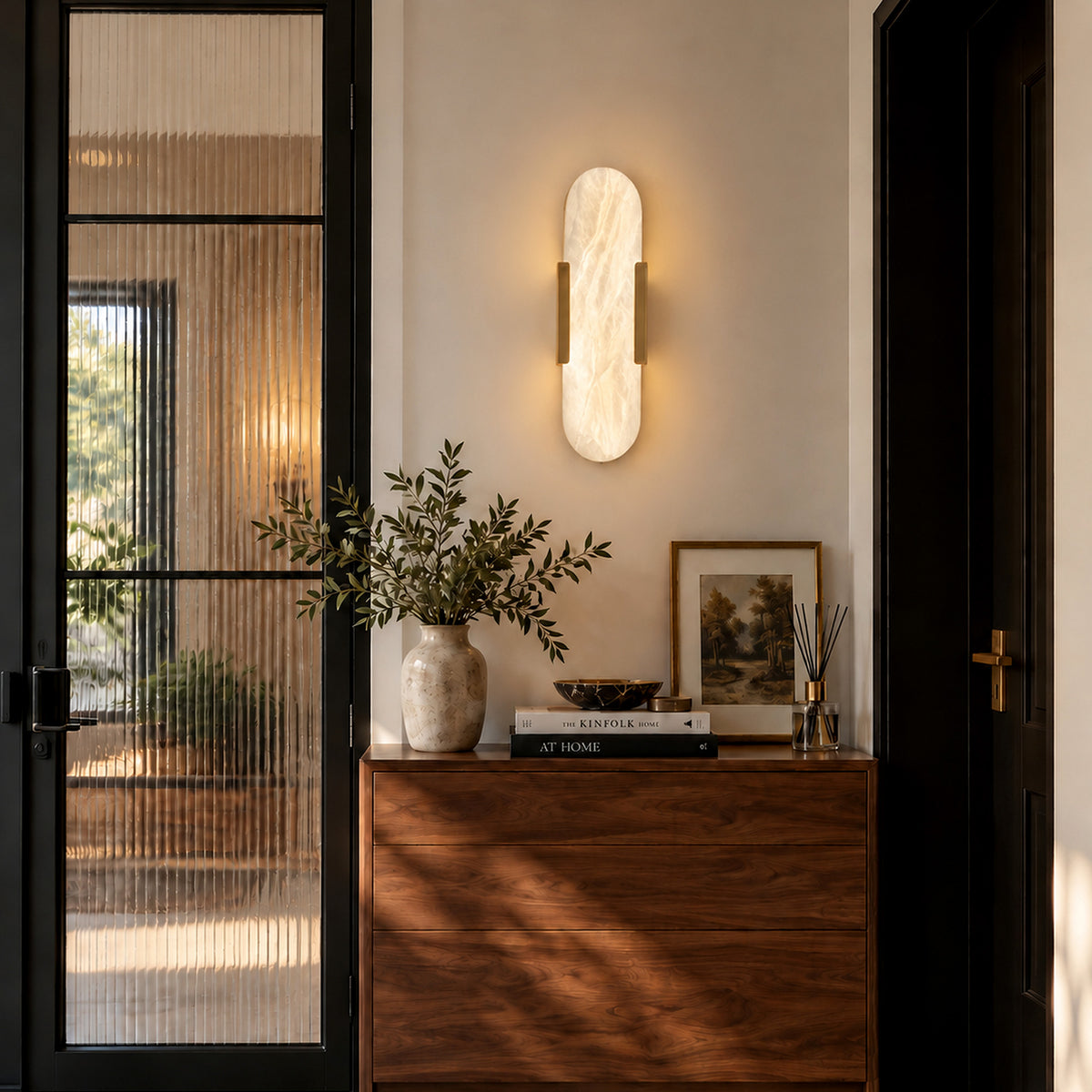 Warmly glowing capsule Spanish alabaster wall light mounted above dark wooden console table in entryway foyer