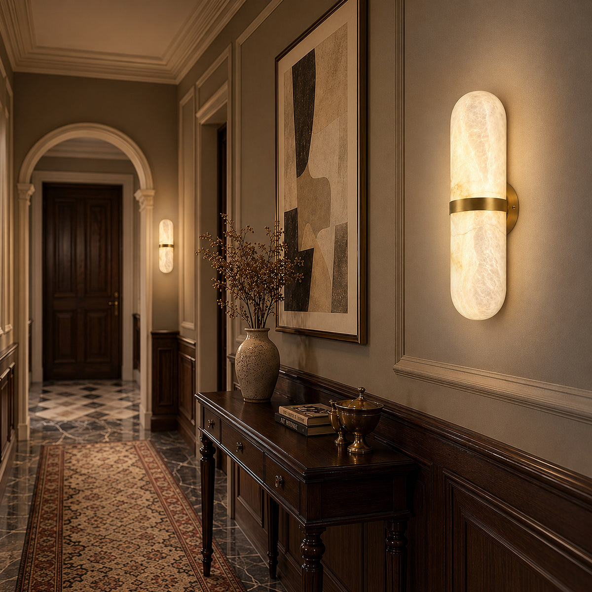 Pair of glowing Spanish natural alabaster capsule wall sconces mounted along a classic hallway with dark wooden console table and artwork