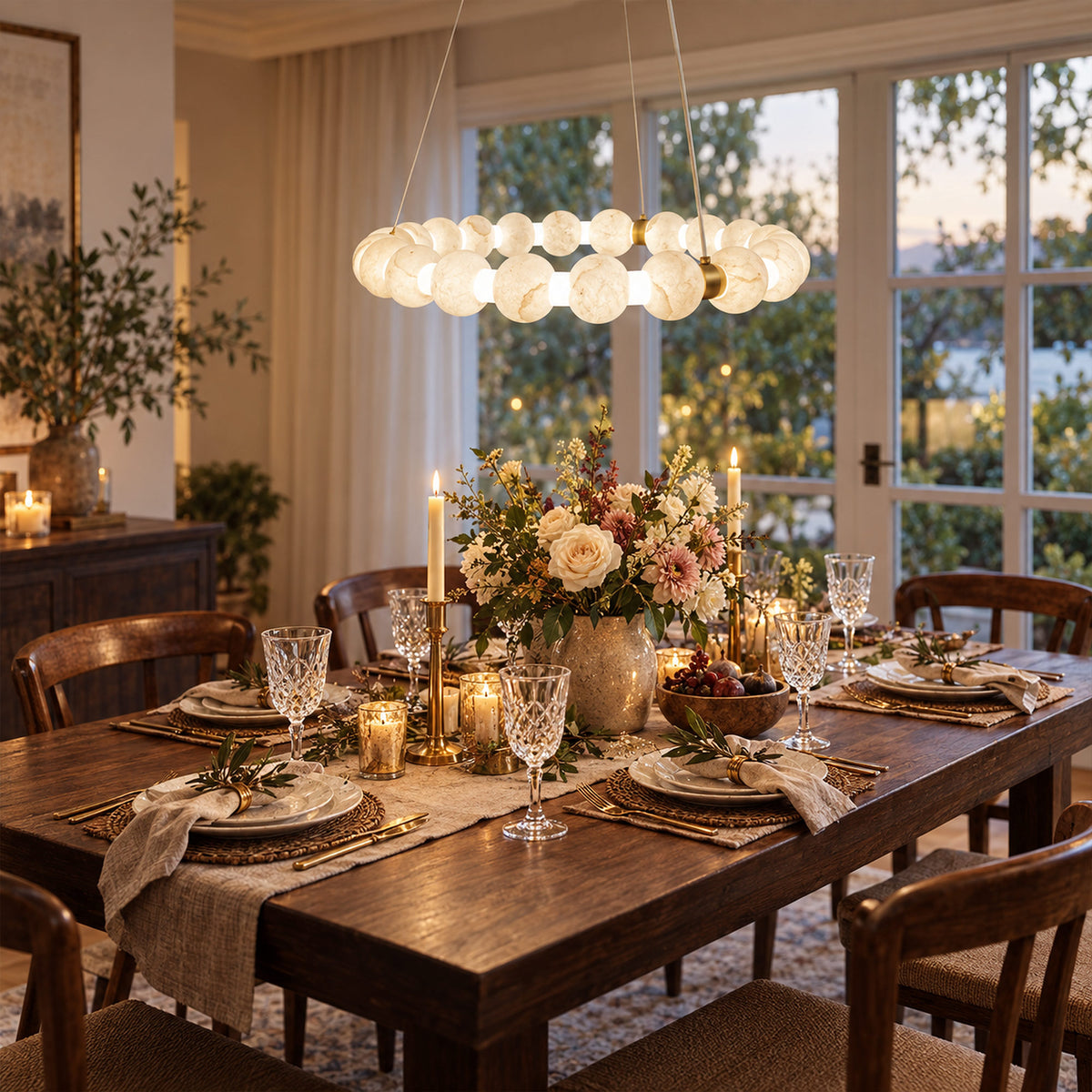Warmly lit Spanish alabaster orb ring pendant light hanging above a rustic wooden dining table set up for dinner