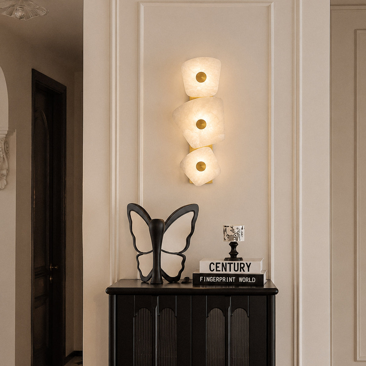 Spanish alabaster stone wall sconce illuminated above black cabinet and decorative butterfly sculpture