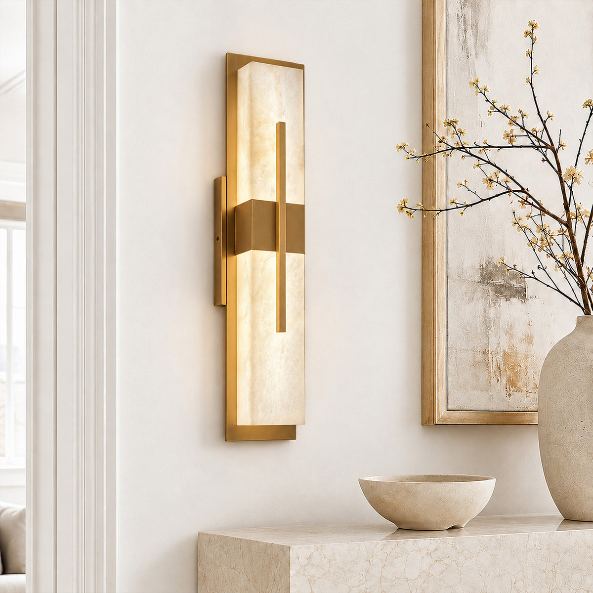 Illuminated rectangular Spanish alabaster wall sconce with brushed brass frame mounted in a bright modern entryway above marble console