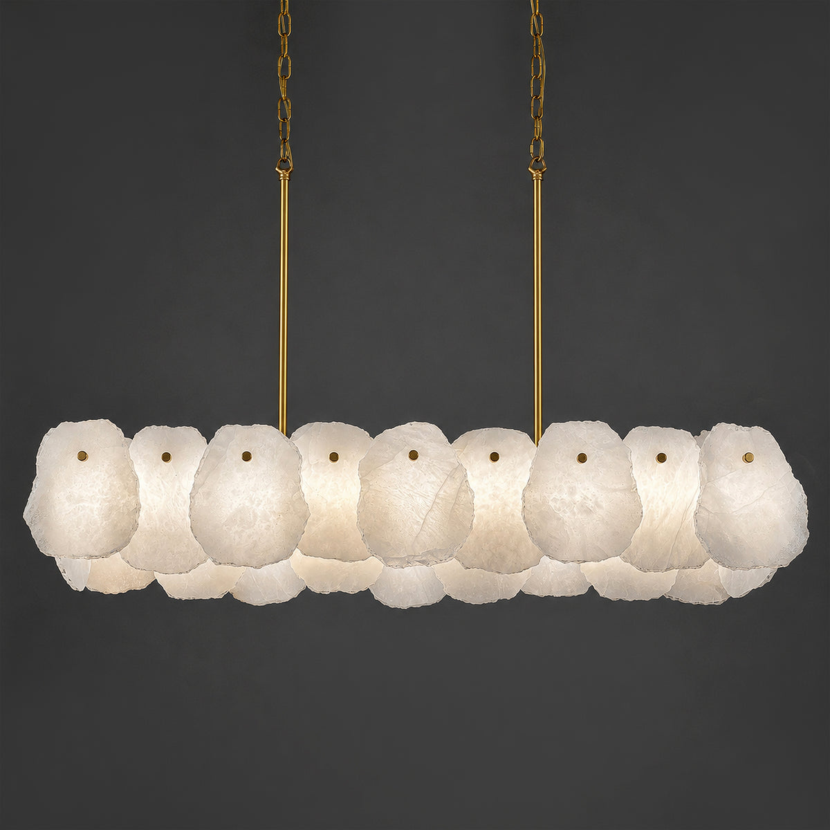 Illuminated Spanish alabaster stone linear chandelier with brass hardware displayed against dark gray background