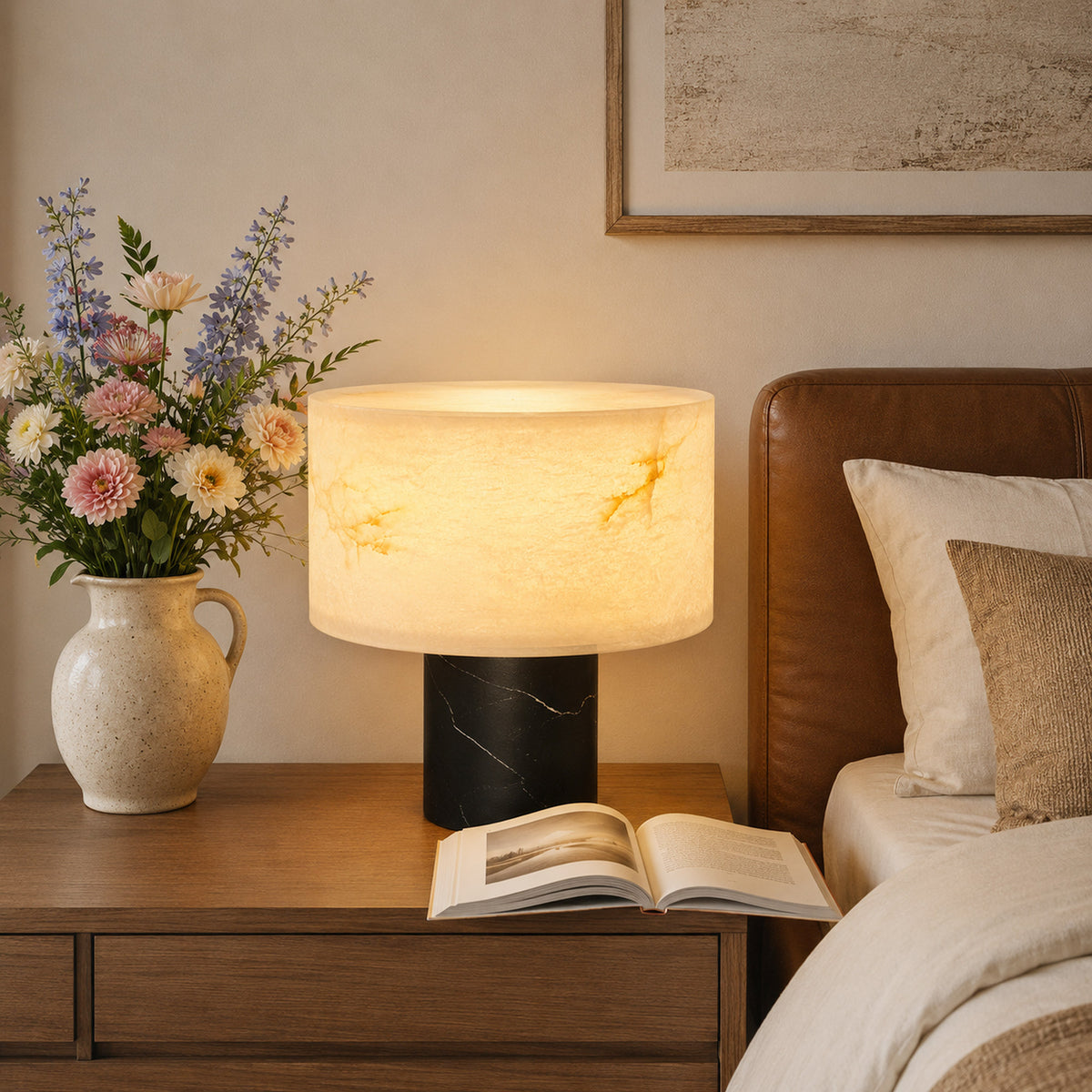 Warm illuminated Spanish alabaster table lamp on wooden nightstand beside cozy bed and fresh flowers