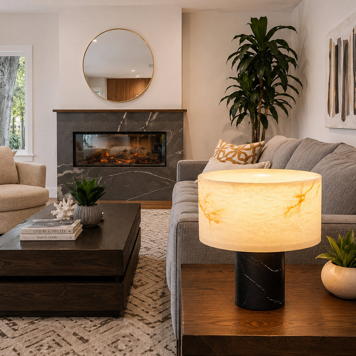 Illuminated alabaster cylinder table lamp on end table next to grey sofa in contemporary living room with fireplace