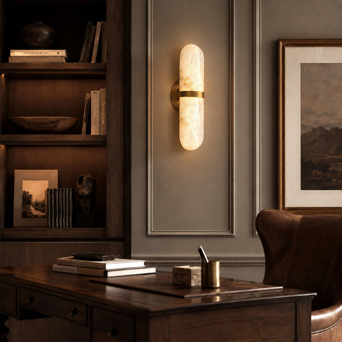 Illuminated Spanish natural alabaster capsule sconce on grey wainscoting wall next to dark wood bookshelves in a study room