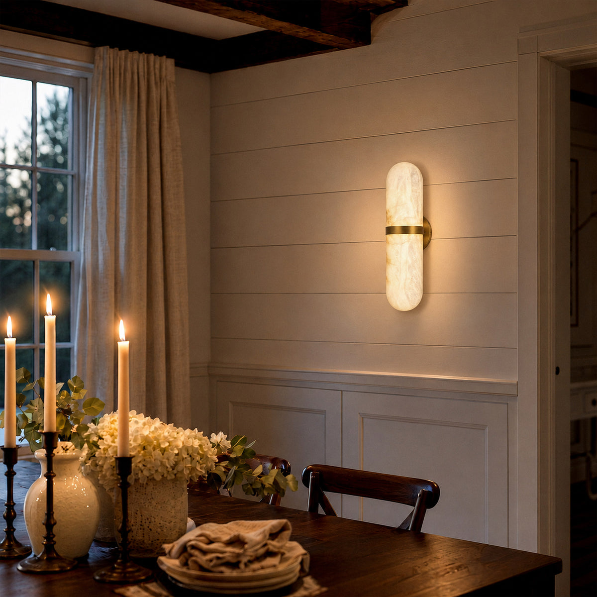 Warmly lit Spanish natural alabaster wall sconce installed on white paneled wall near a wooden dining table with candles