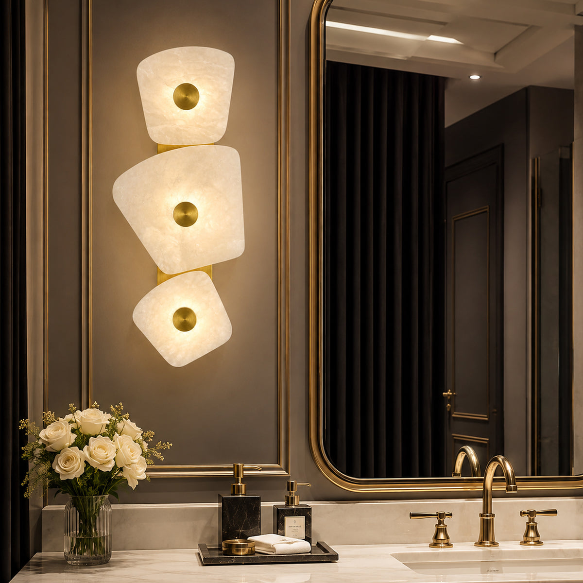 Organic Spanish alabaster stone wall sconce glowing beside large brass framed vanity mirror on marble countertop in luxury bathroom