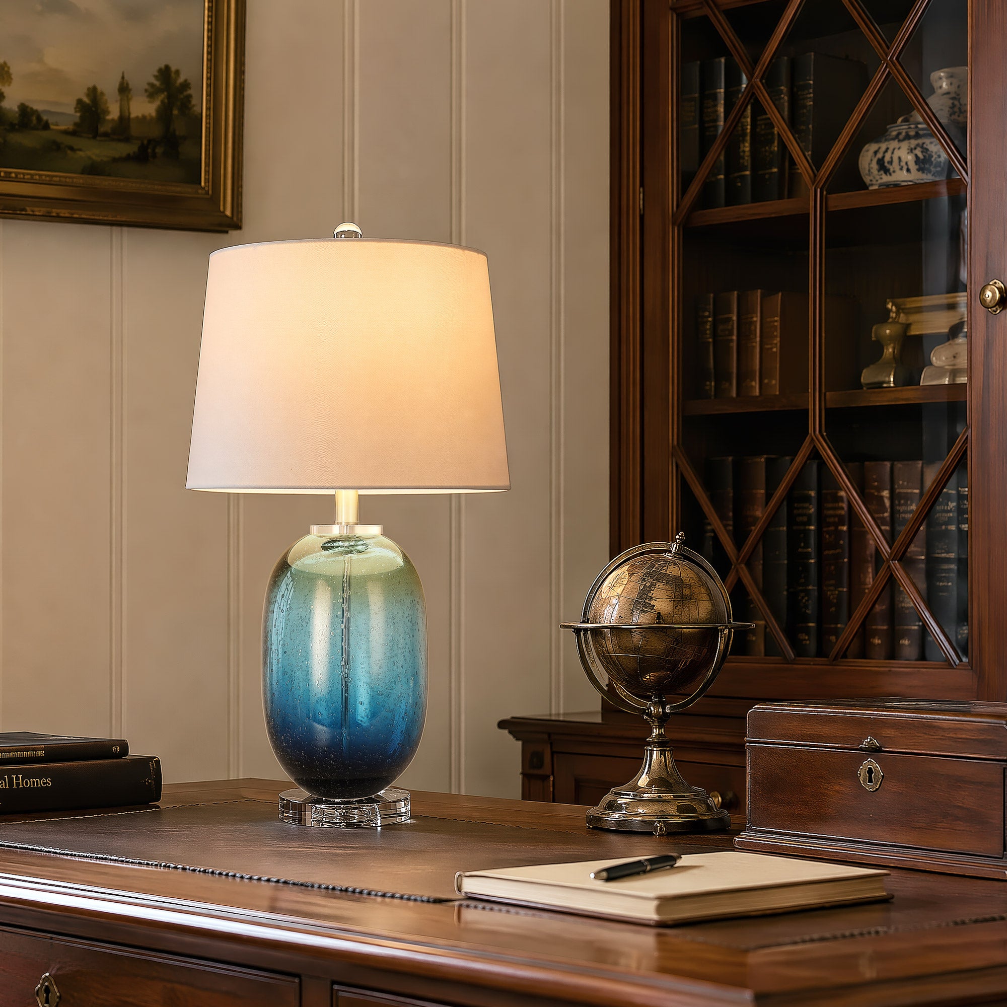 Murano style cylindrical blue art glass table lamp providing ambient task lighting on a vintage dark wood executive desk in a classic home library