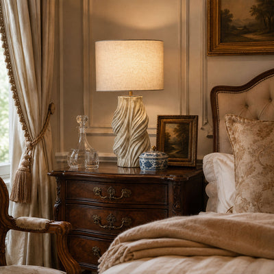 Vintage handmade ceramic table lamp lit on wooden nightstand in classic elegant bedroom setting