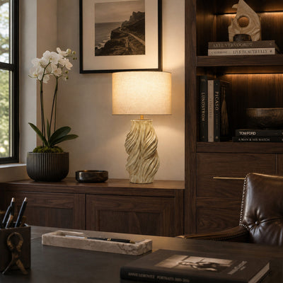 Illuminated artisan ceramic table lamp placed on dark wood cabinet next to modern bookshelf