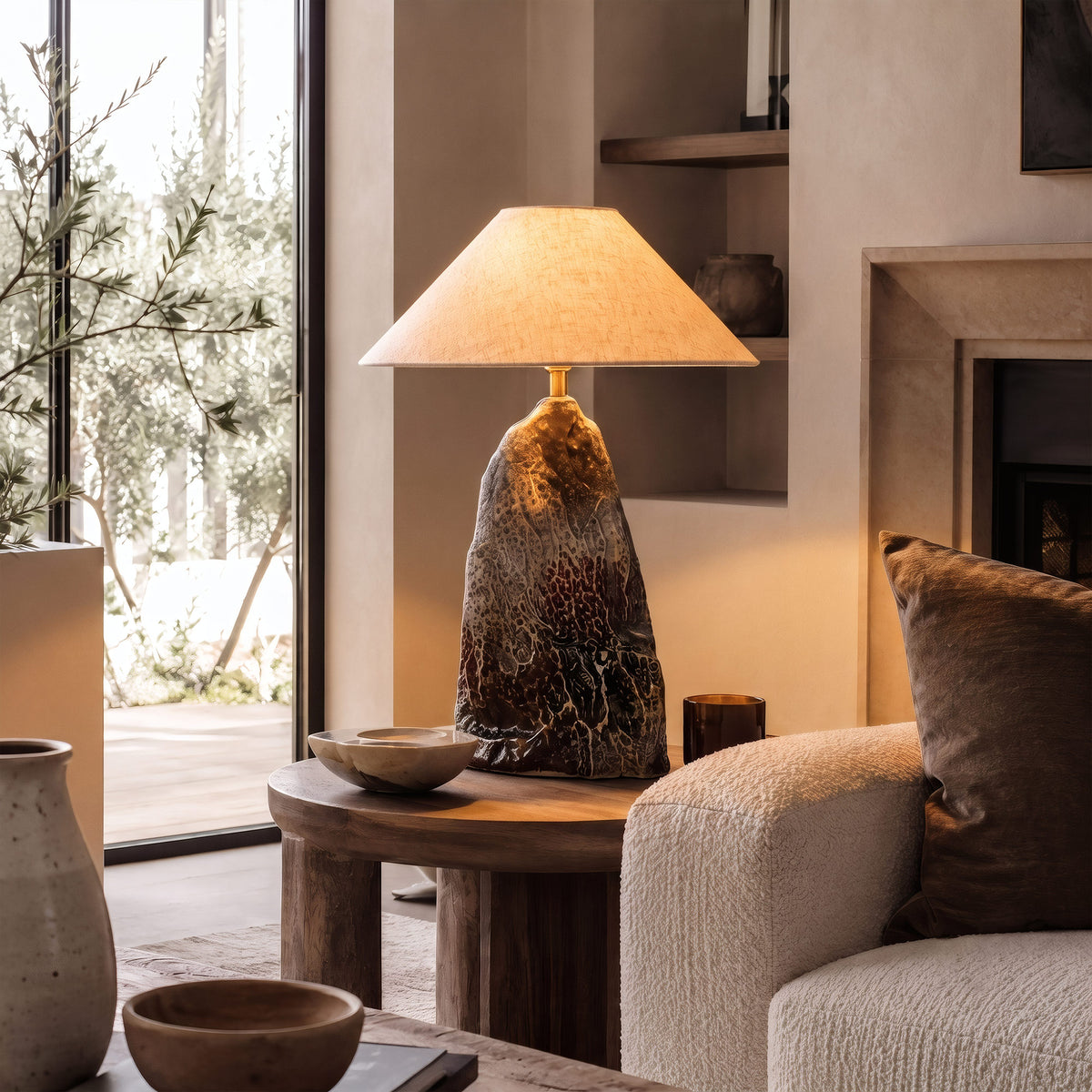 Warmly lit rockery flambe glaze ceramic table lamp placed on a rustic wooden side table next to a modern cream sofa.