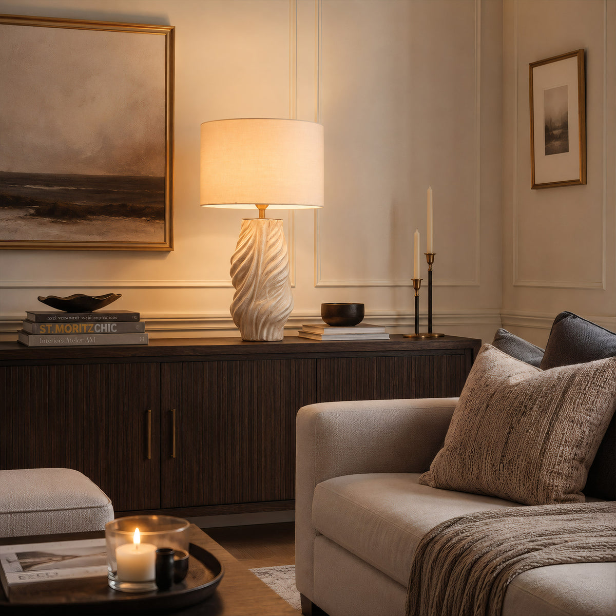A glowing white grey fluted ceramic table lamp providing warm accent lighting on a dark wood console table behind a beige sofa